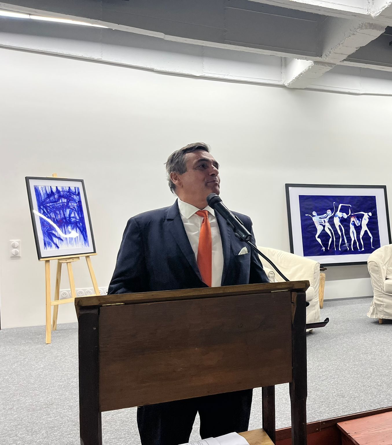 Un intervenant au pupitre devant des œuvres bleues, photographie publiée par la paroisse.