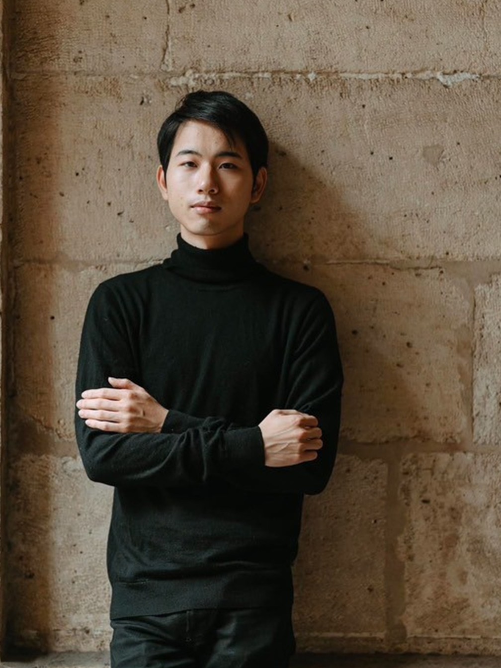Portrait du pianiste Kazumitsu Ujisawa devant un mur de pierre.
